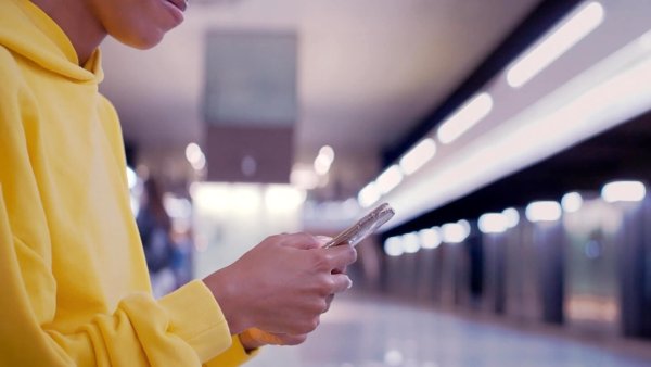 Eine Frau steht mit Handy an einer U-Bahn-Station