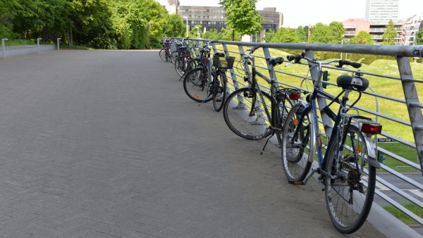 mehrere Fahrräder lehnen in einer Reihe auf einer Brücke am Geländer