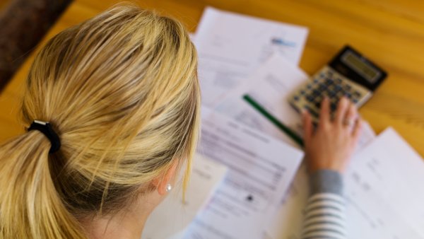 Das Foto zeigt eine Frau, die am Schreibtisch mit Taschenrechner und Formularen arbeitet.