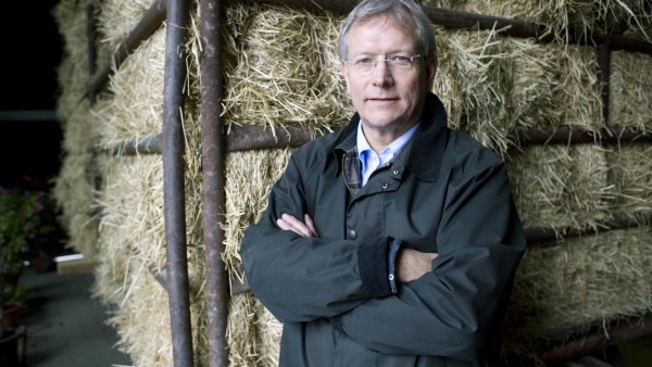 Eckhard Uhlenberg in dunkler Jacke mit verschränkten Armen vor Heuballen stehend.