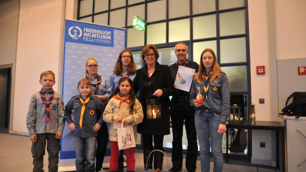 Auf dem Foto ist Ministerin Ute Schäfer gemeinsam mit Kindern und Jugendlichen zu sehen, die das Friedenslicht aus Betlehem überreichen.
