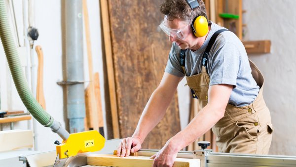 Das Bild zeigt einen Handwerker an einer industriellen Holzschneidemaschine.