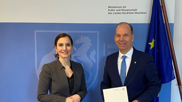 eine Frau und ein Mann stehen vor einem blauen Hintergrund, der Mann hält ein Dokument in beiden Händen