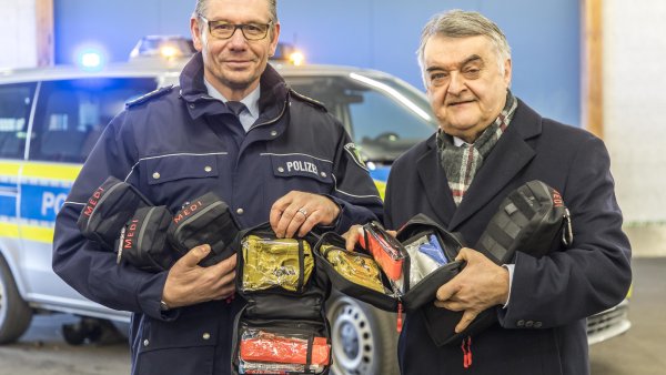 Minister Reul überreicht Medipacks an Dietmar Henning von der Polizei Düsseldorf. Im Hintergurnd steht ein Polizeiwagen.