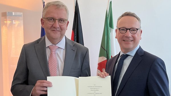 Minister Dr. Limbach rechts im schwarzen Anzug übergibt Klaus Georg Müller im grauen Anzug mit roter Krawatte eine Urkunde