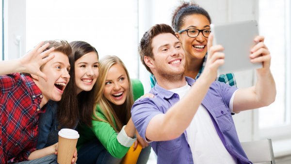 Das Foto zeigt mehrere lachende Jugendliche, die ein Selfie aufnehmen.