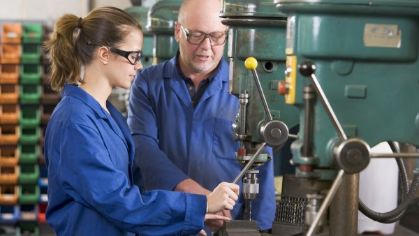 Auf diesem Foto zu erkennen sind ein weiblicher Lehrling mit Ausbilder an einer Maschine