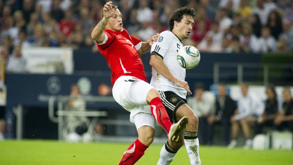 2 Fußballspieler im Zweikampf um den Ball, im Hintergrund eine vollbesetzte Tribüne.