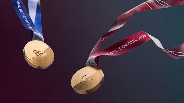 zwei Goldmedaillen der olympischen Winterspiele in Mailand. Zu sehen sind auf beiden die 5 olympischen Ringe auf Gold, die linke Medaille hat ein blau-weißes Band, die recht ein rot-weißes.