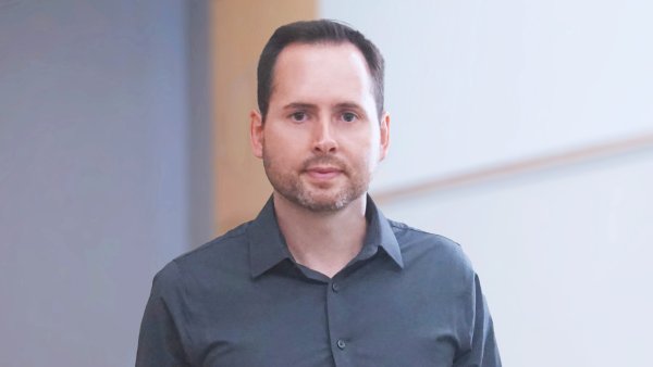 ein Mann mit kurzen dunklen Haaren und dunkelgrauem Hemd 