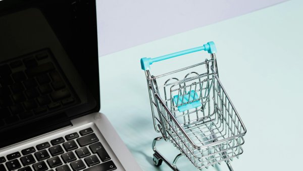 Neben einem Laptop steht ein Miniatur-Einkaufswagen