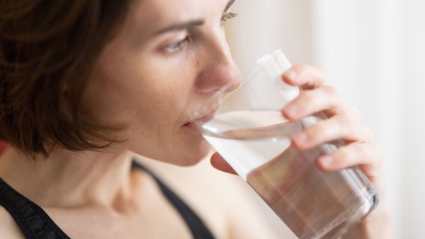 Eine Frau mit schulterlangen, dunklen Haaren und einem schwarzen Tanktop trinkt ein Glas Wasser