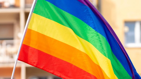 Fahne in Regenbogenfarben, im Hintergrund leicht verschwommen ein gelbes Mehrfamilienhaus