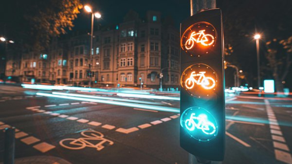 Kreuzung mit beleuchteter Fahrradampel im Fokus, bei Nacht, Verkehr nur als leuchtende Linien im Hintergrund