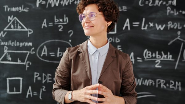 eine Frau in braunem Blazer vor einer Tafel voller mathematischer Formeln