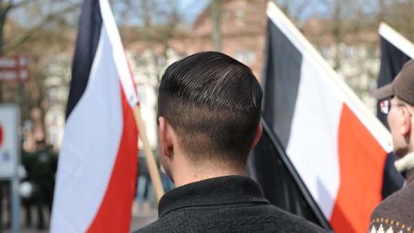 verschiedene Personen stehen mit dem Rücken zum Bild und Fahnen in der Hand zusammen. Die Fahne hat einen schwarzen, einen weißen und einen roten Streifen und symbolisiert die Reichsflagge