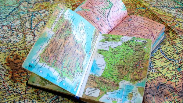 2 aufgeschlagene Landkartenbücher liegen auf einer großen Landkarte, die sich über das gesamte Bild erstreckt.