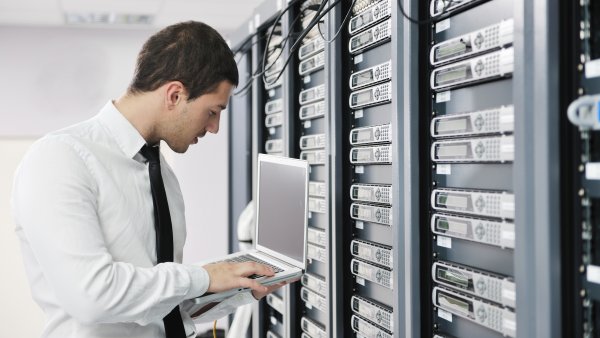 Ein Techniker in weißem Hemd und schwarzer Krawatte vor einer Wand voller Server.