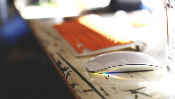 Orangene Tastatur und Maus auf einem Tisch im Sonnenschein