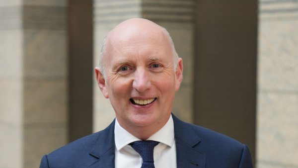 ein Mann in blauem Anzug, weißem Hemd und blauer Krawatte lächelt