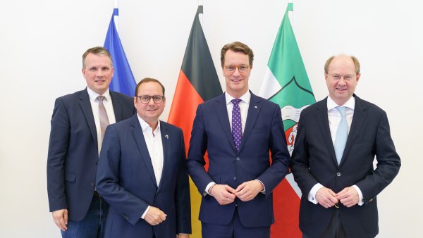 Von links nach rechts stehen Bürgermeister Tobias Stockhoff, Oberbürgermeister Thomas Kufen, Ministerpräsident Hendrik Wüst und Landrat Dr. Olaf Gericke gemeinsam vor den Flaggen der Europäischen Union, Deutschlands und Nordrhein-Westfalens. Die vier Politiker tragen dunkle Anzüge und blicken in die Kamera.
