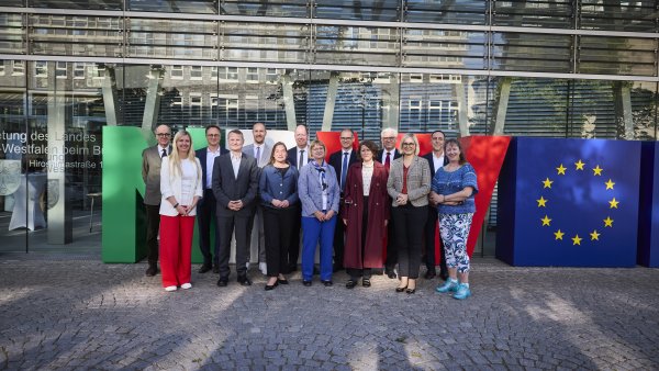 Eine Gruppe menschen steht vor riesigen Buchstaben N R und W und einem Würfel mit dem Europa-Logo