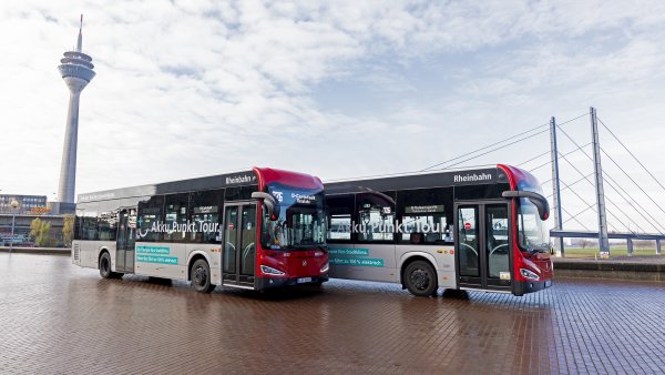 Zwei Busse stehen am Rheinufer mit dem Rheinturm und der Rheinkniebrücke im Hintergrund