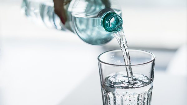 Eine Hand gießt aus einer Flasche Wasser in ein Glas.