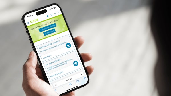 Eine Hand hält ein Handy, darauf zu sehen die „MeinELSTER+“-App