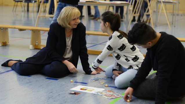 Ministerpräsidentin Hannelore Kraft sitzend auf dem Turnhallenboden mit Schülerinnen und Schülern mit Themenpuzzle 