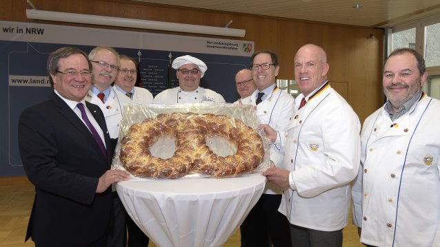Ministerpräsident Armin Laschet und eine Gruppe von Bäckern stehen an einem Tisch mit einer großen Brezel