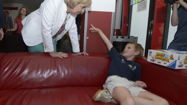 Ministerpräsidentin Hannelore Kraft beugt sich über ein Couch, auf dem ein behinderter Junge sitzt