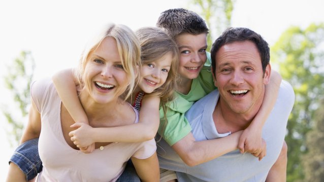 Auf dem Bild sind eine Mutter und ein Vater zu erkennen, die jeweils ein kleines Mädchen und einen kleinen Jungen auf ihren Schultern tragen.