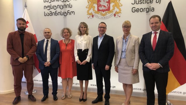 vier Männer und drei Frauen stehen vor einer Wand mit dem georgischen Wappen und einer Deutschland-Fahne