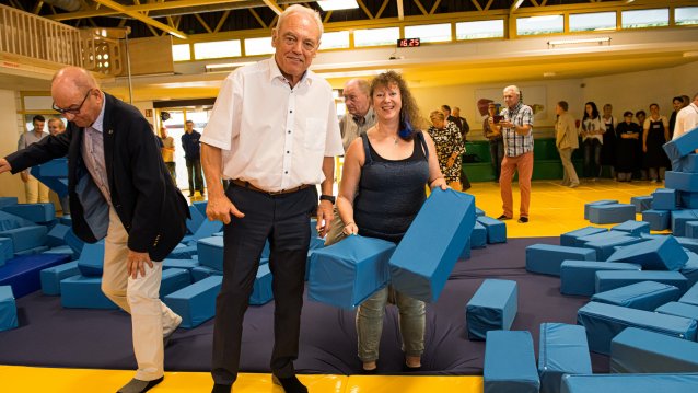 Staatssekretärin Milz mit dem Präsidenten des Landessportbundes NRW, Herrn Walter Schneeloch, an einer Schnitzelgrube gefüllt mit großen, blauen, gepolsterten Quadern.