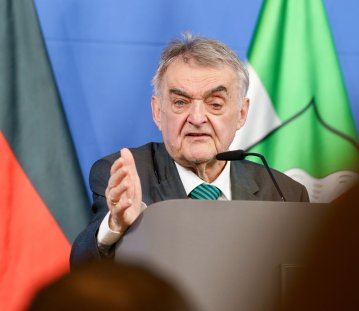 Minister Reul spricht an einem Rednerpult vor Flaggen