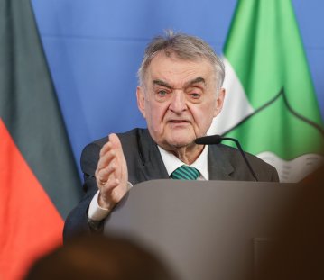 Minister Reul spricht an einem Rednerpult vor Flaggen