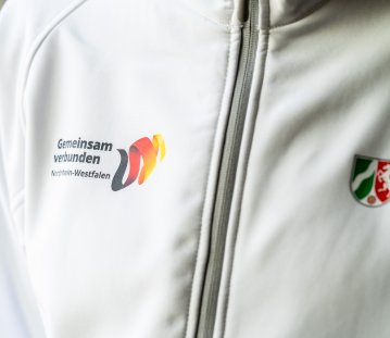 Ein Close-Up einer weißen Sportjacke mit dem NRW-Wappen und dem Logo von Gemeinsam verbunden