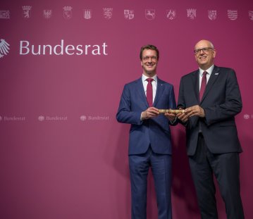 Zwei Männer in Anzügen halten gemeinsam einen Holzstab fest.