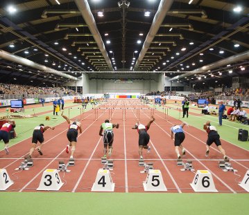 Von hinten betrachtet: Sieben Sprinter starten gerade zum Sprint in einer Indoor-Leichtathletikhalle.