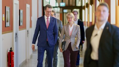 Ministerpräsident Hendrik Wüst und Ministerin Feller gehen auf einem Flur zur Pressekonferenz