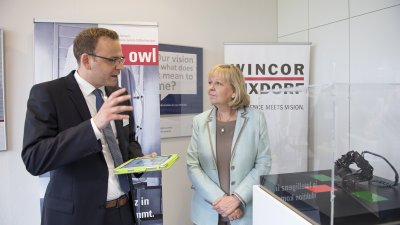 Ein Mitarbeiter zeigt der Ministerpräsidentin etwas vor einem Schaukasten