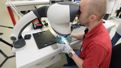 Ein Mitarbeiter betrachtet eine Platine unter einem Mikroskop