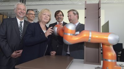 Ministerpräsidentin Kraft betrachtet einen orangenen Roboterarm