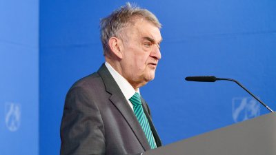 Minister Reul spricht an einem Rednerpult vor Flaggen