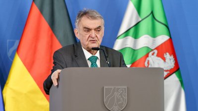 Minister Reul spricht an einem Rednerpult vor Flaggen