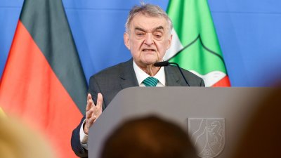 Minister Reul spricht an einem Rednerpult vor Flaggen