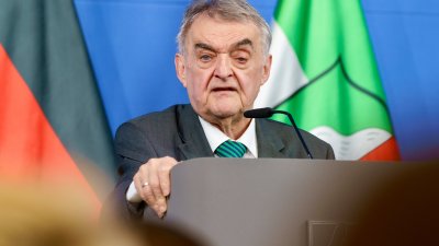 Minister Reul spricht an einem Rednerpult vor Flaggen