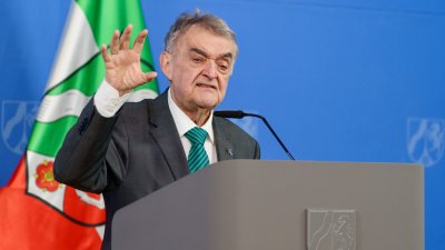 Minister Reul spricht an einem Rednerpult vor Flaggen