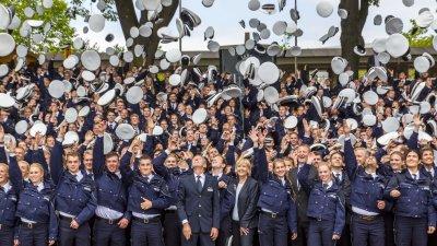 Polizistenanwärter werfen ihre Mütze in die Luft, mittig stehen Ministerpräsidentin Hannelore Kraft und dahinter Innenminister Ralf Jäger